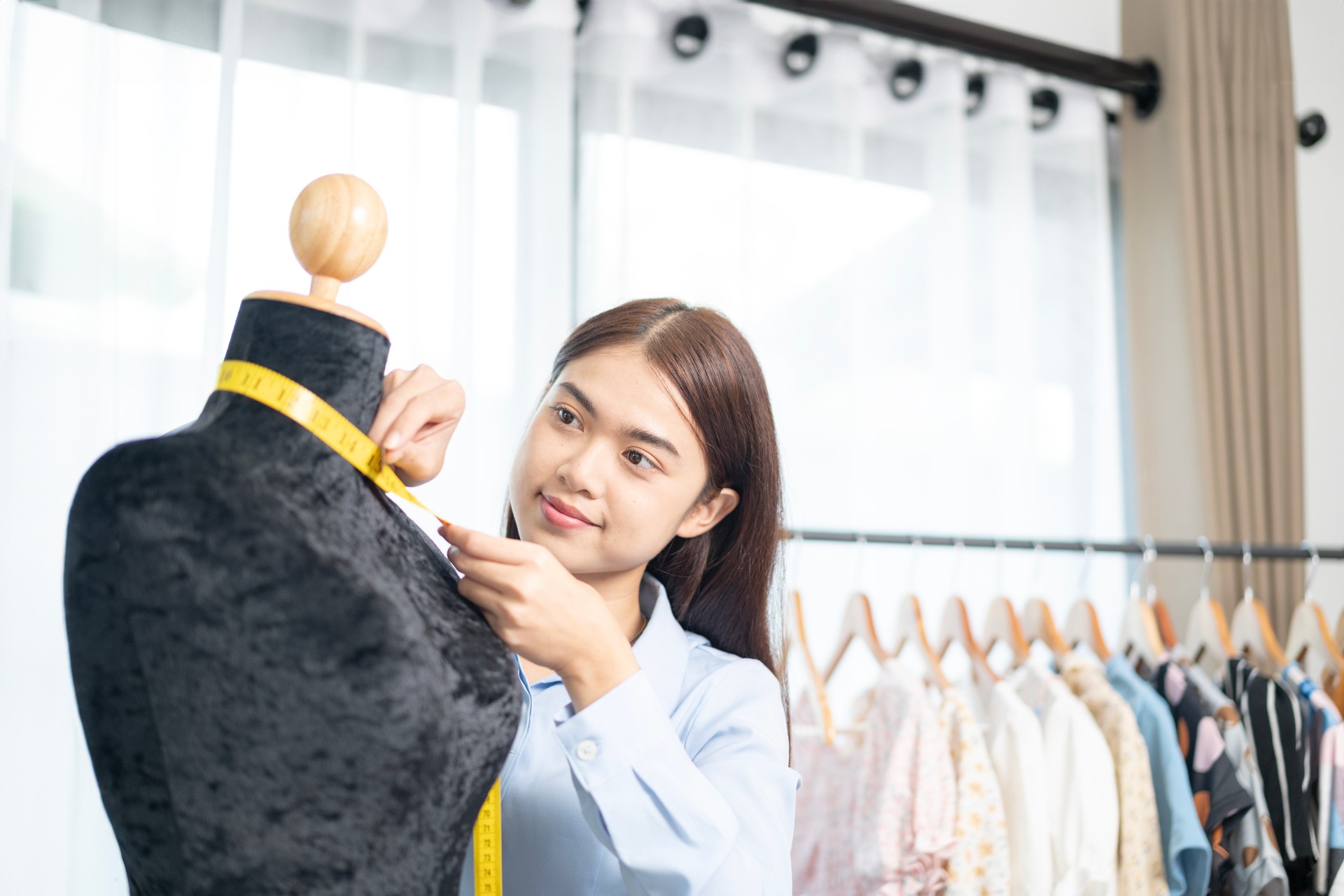 The female designer is working on measuring the dimensions of a mannequin for a dress